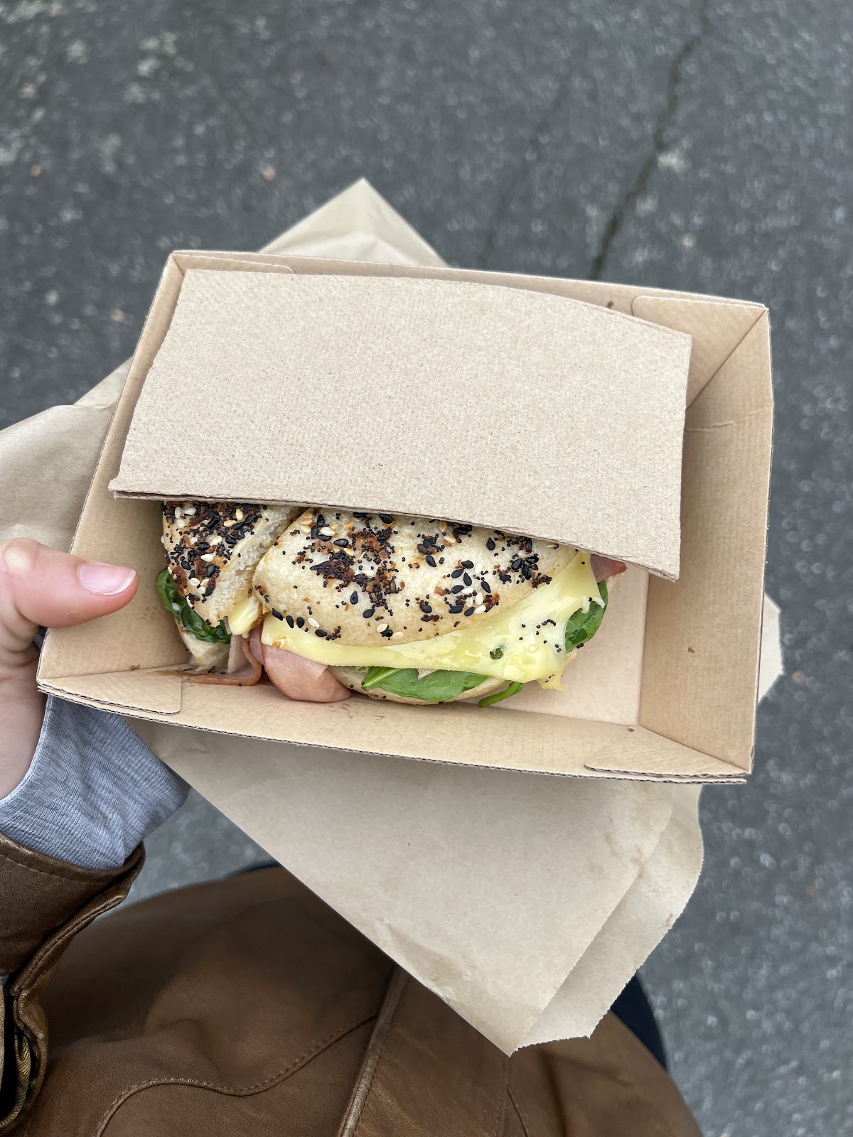 Seeded bagel with melted cheese in a takeaway box